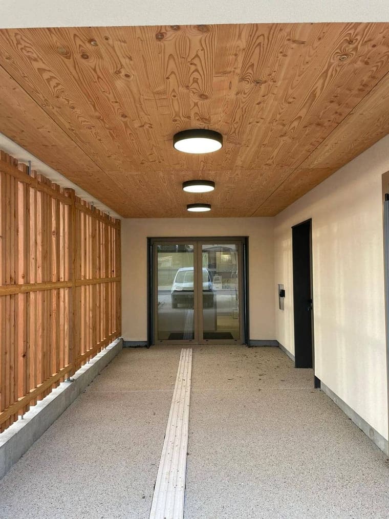 Entrée couverte d'un immeuble, plafond bois et hublots au plafond